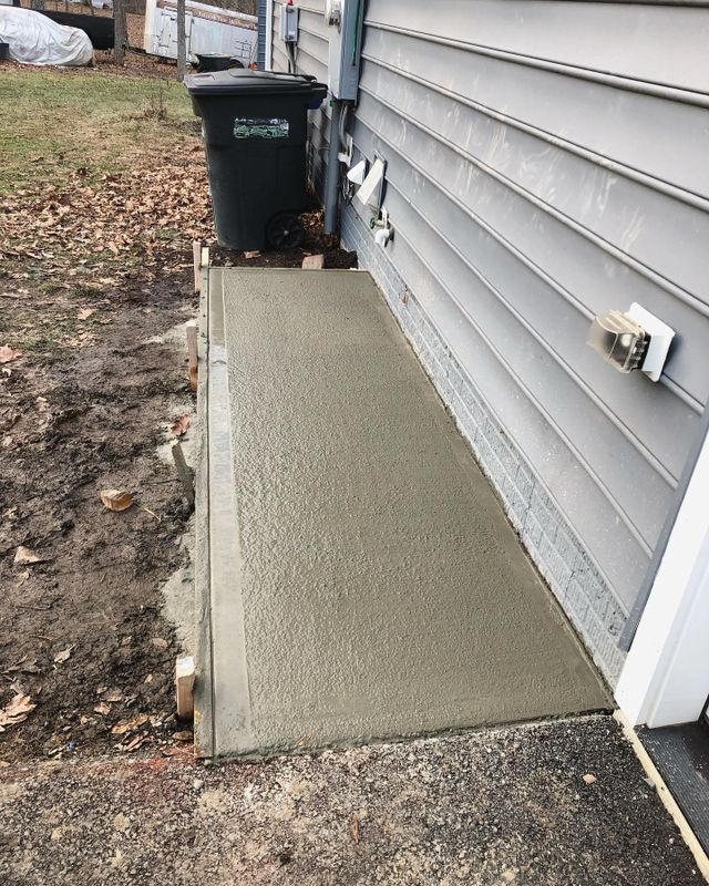 Concrete side walkway beside gray house siding with utility meters and a trash bin.