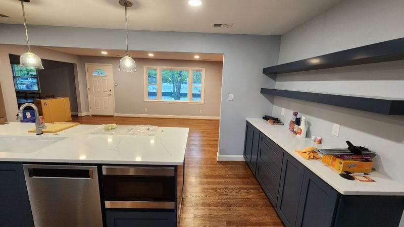 Modern kitchen with white island, dark cabinets, wood floors, and open shelves