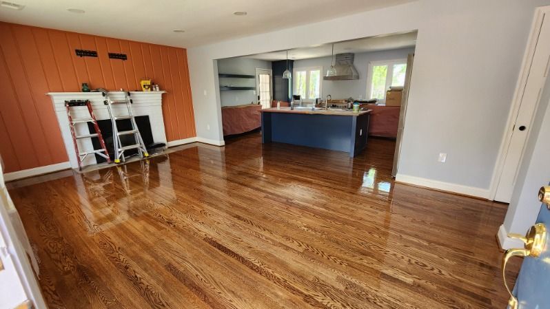 Empty living room with glossy hardwood floors and a kitchen opening in the background