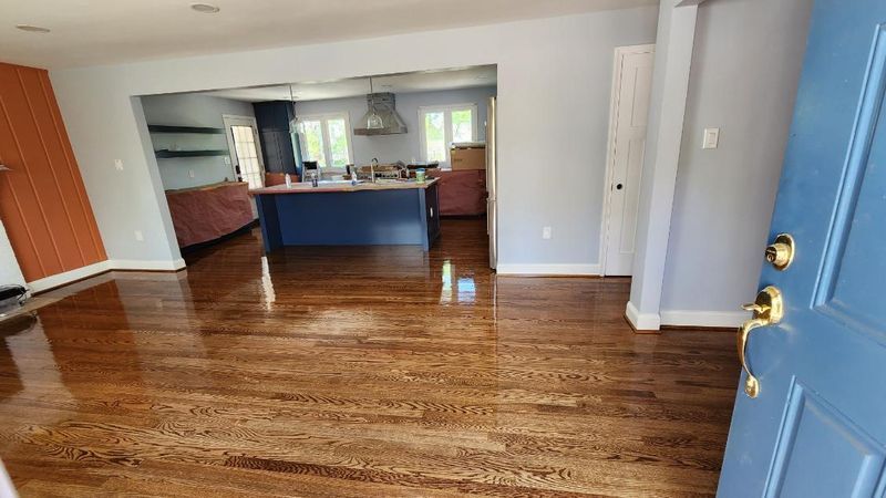 Empty living room with glossy hardwood floors, open kitchen, and a blue front door
