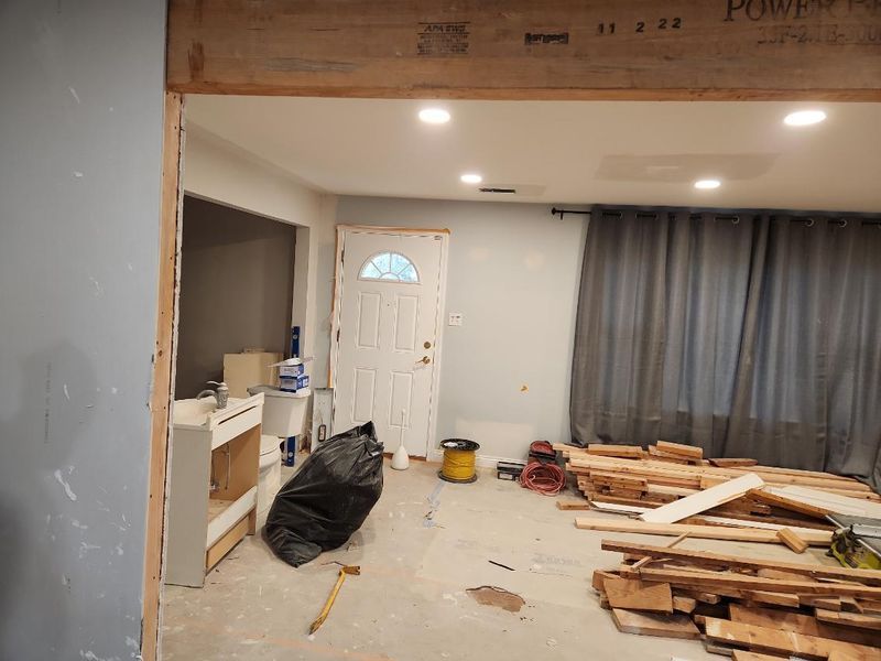 Partially renovated room with drywall, tools, lumber piles, and a white door beside gray curtains.