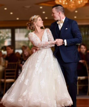 Bride and groom dancing at wedding reception. Bride in white gown, groom in navy suit.