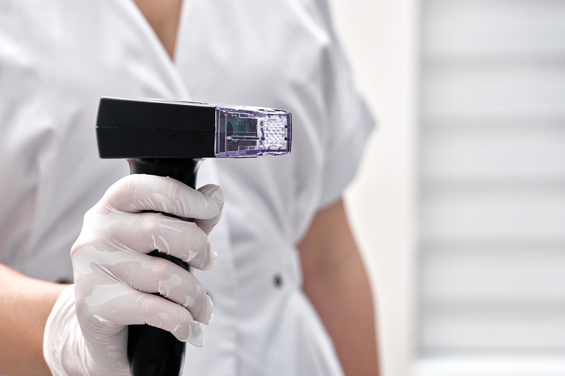 Gloved hand holding a black handheld UV sanitizer over a white shirt background