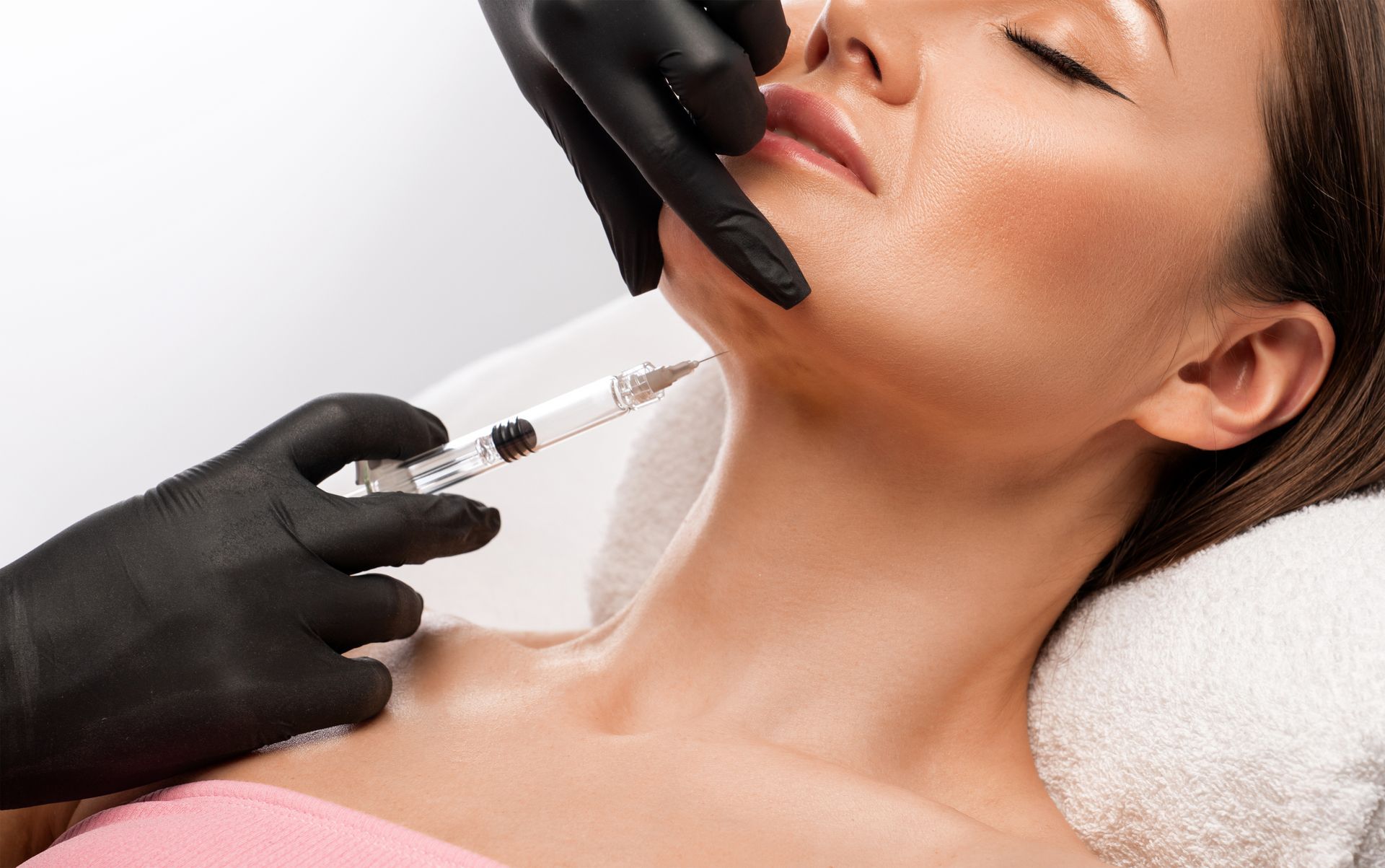Gloved hands injecting a woman's chin with a syringe during a cosmetic facial treatment
