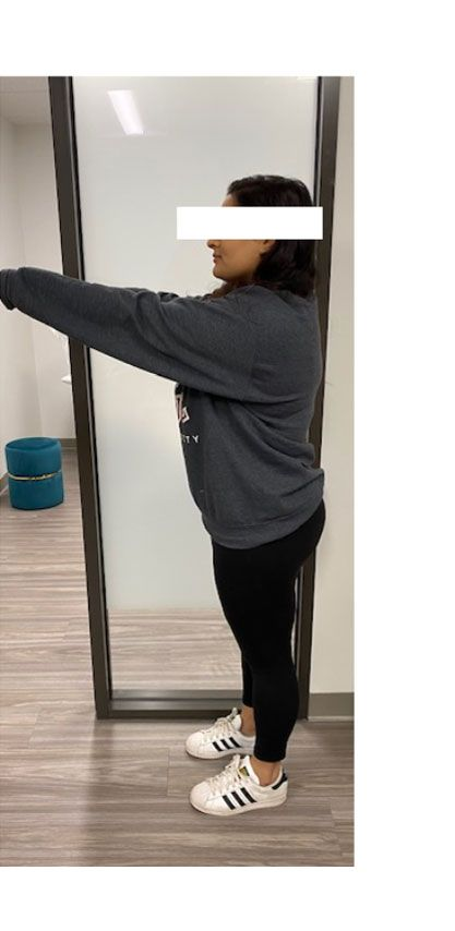 Person in a gray sweatshirt and black leggings, standing with arms outstretched, near a mirror.