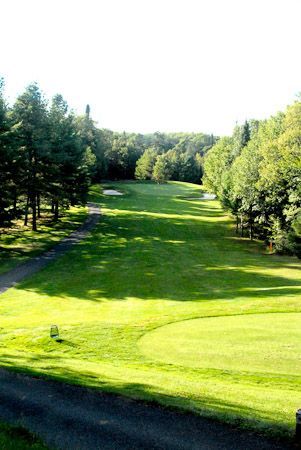 A scenic view down a lush green golf course fairway lined with dense trees, leading to a distant green and sand traps.