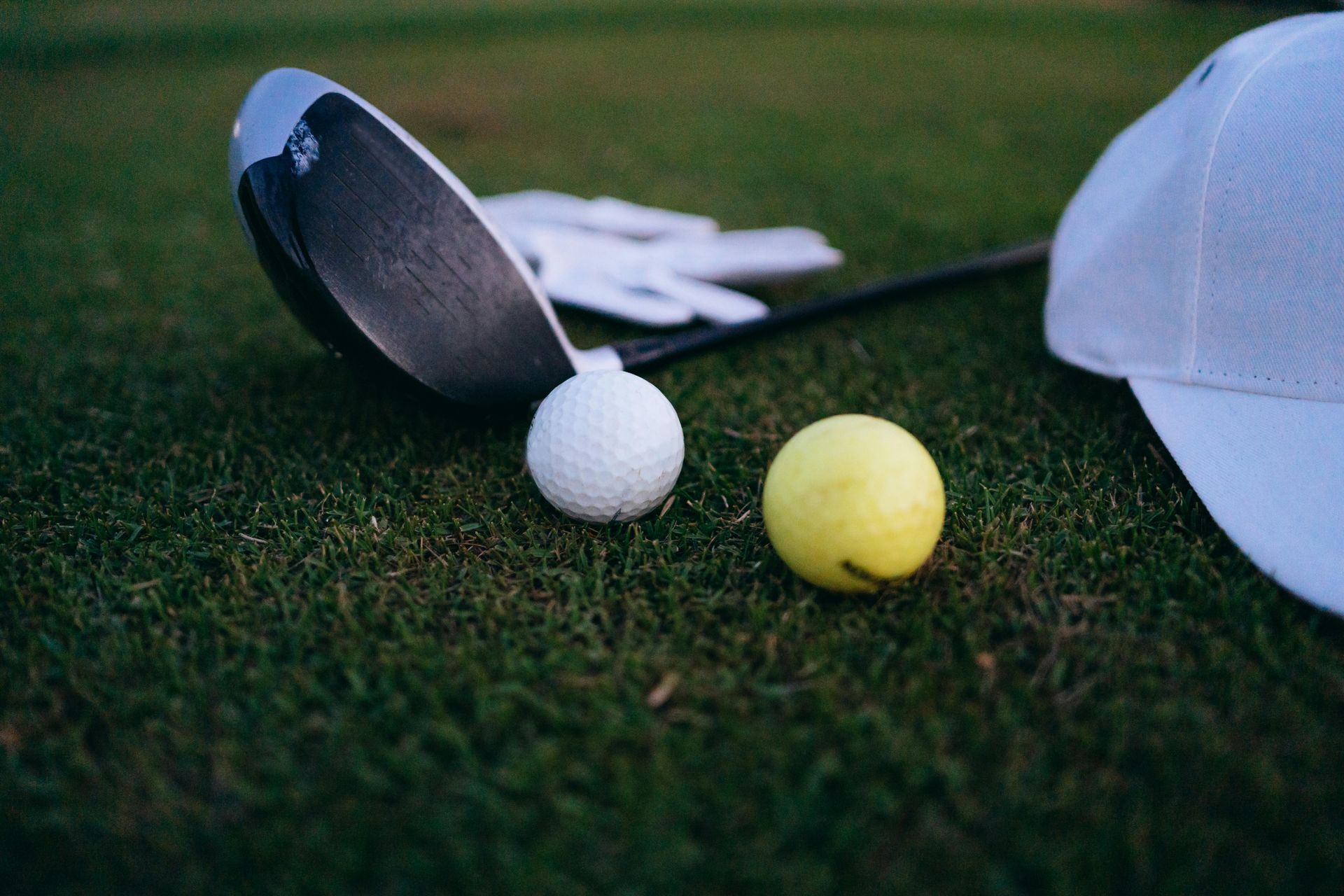 Golf clubs, white and yellow balls on green grass beside a white cap
