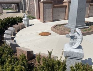 Stone memorial area with a circular plaque, engraved benches, and landscaped bushes near a building