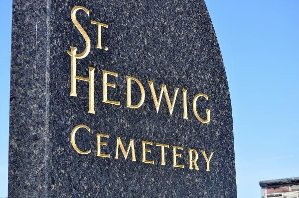 St. Hedwig Cemetery sign on a dark stone pillar against a blue sky