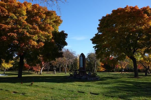 Autumn park with colorful trees framing a stone monument on a sunny green lawn