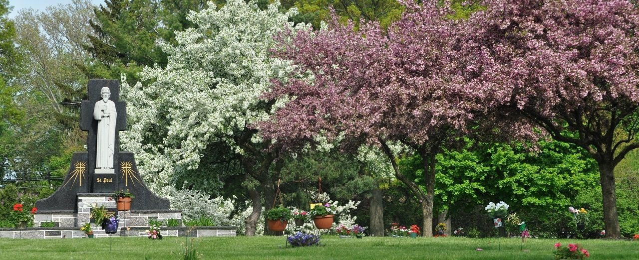 Statue in a lush park with blooming pink and white trees and a green lawn