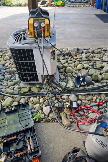 Damaged HVAC unit with exposed wiring and tools on a rocky outdoor surface