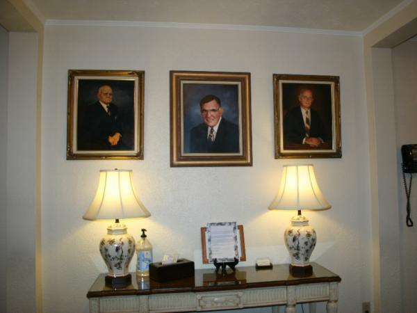 Three portraits of men are hanging on a wall above a table