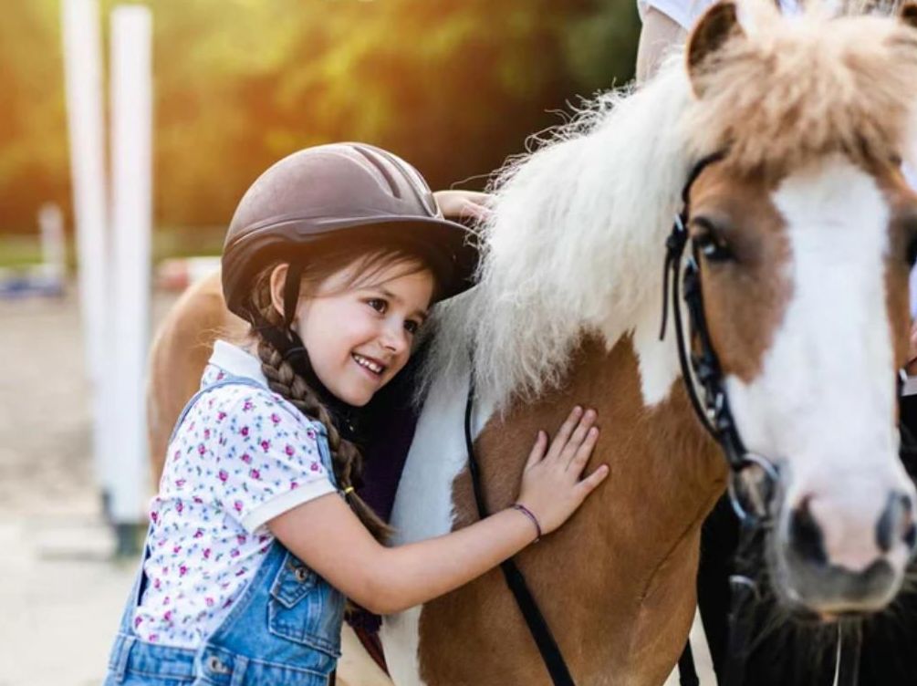 Una bambina accarezza un pony mentre indossa un casco.