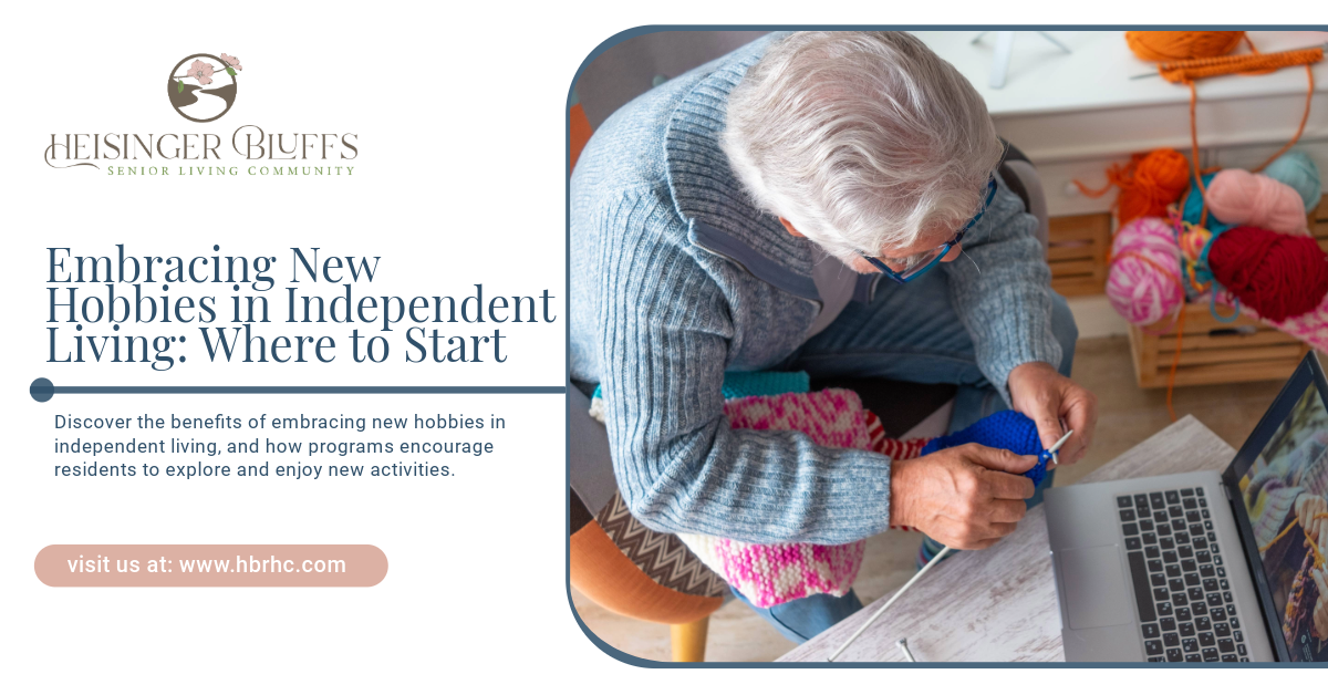 An elderly woman is sitting at a table with a laptop and knitting.