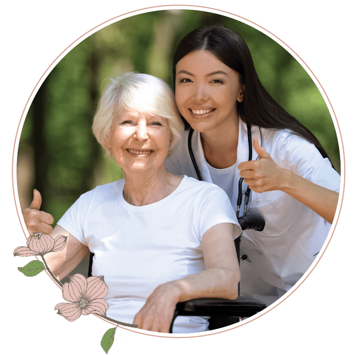 A nurse standing next to an elderly woman on a wheelchair giving a thumbs up 