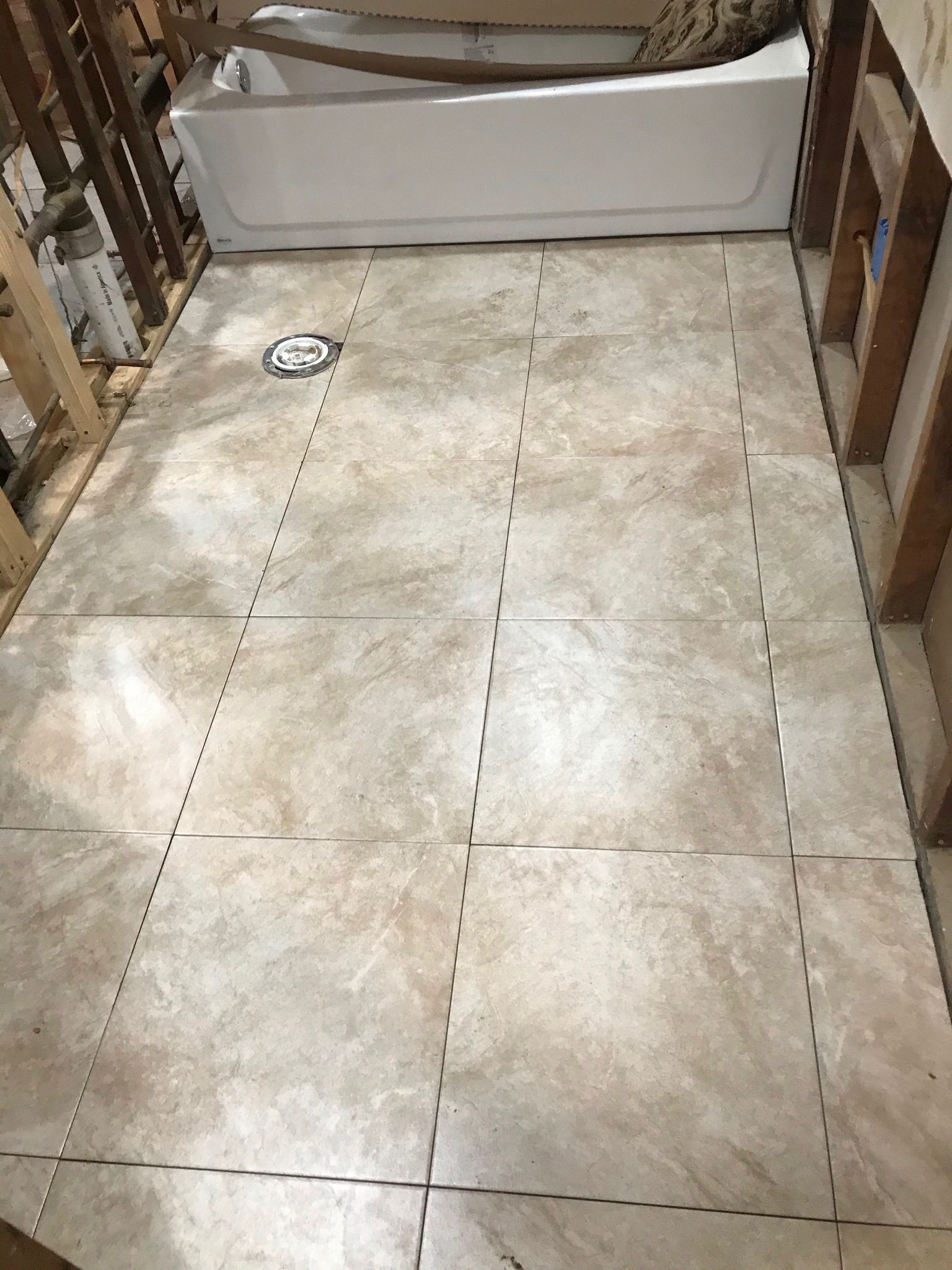 Bathroom floor tiled in beige with a tub in the background. Framing is visible on both sides.