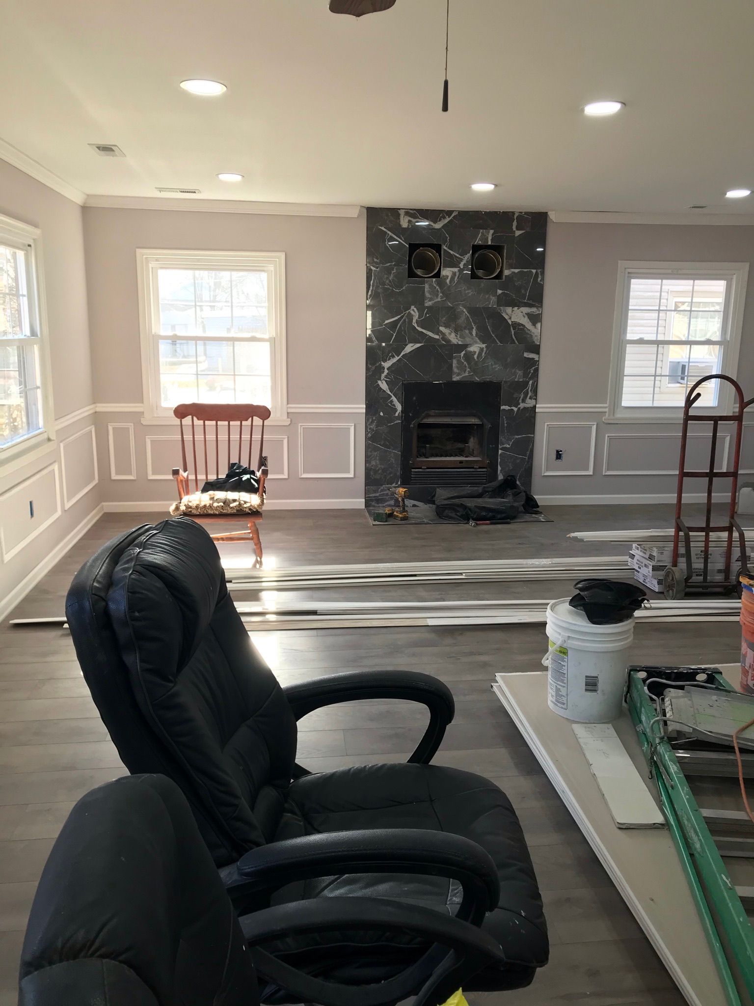 An office chair in front of a fireplace with a black marble surround, near windows, under construction.
