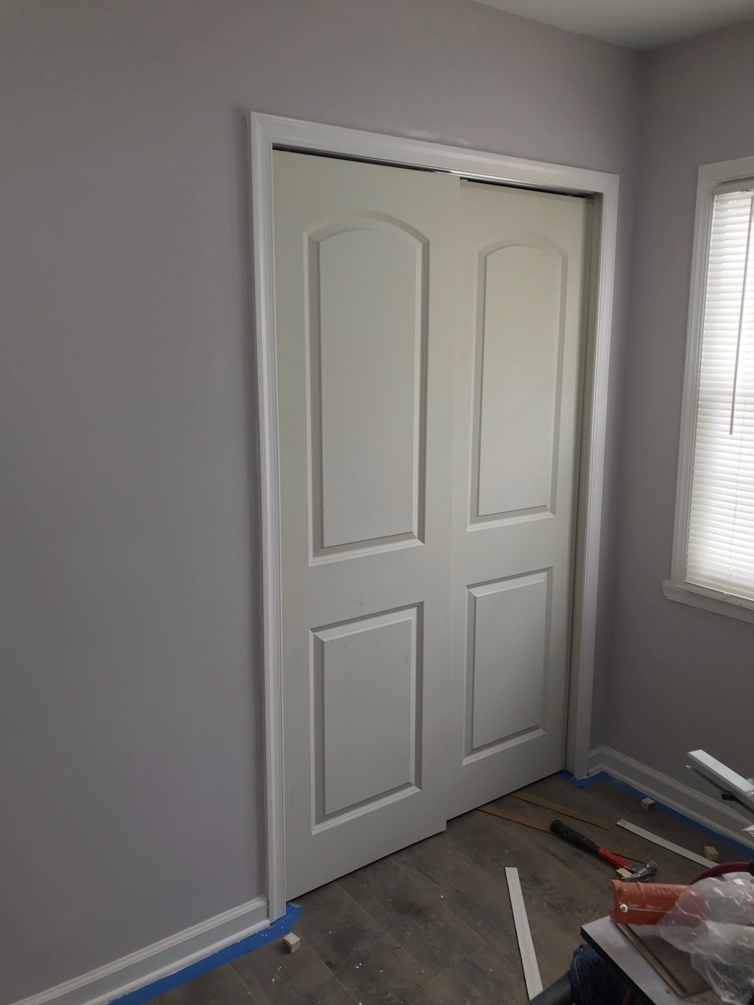 White closet doors in a room with gray walls and a window with blinds.