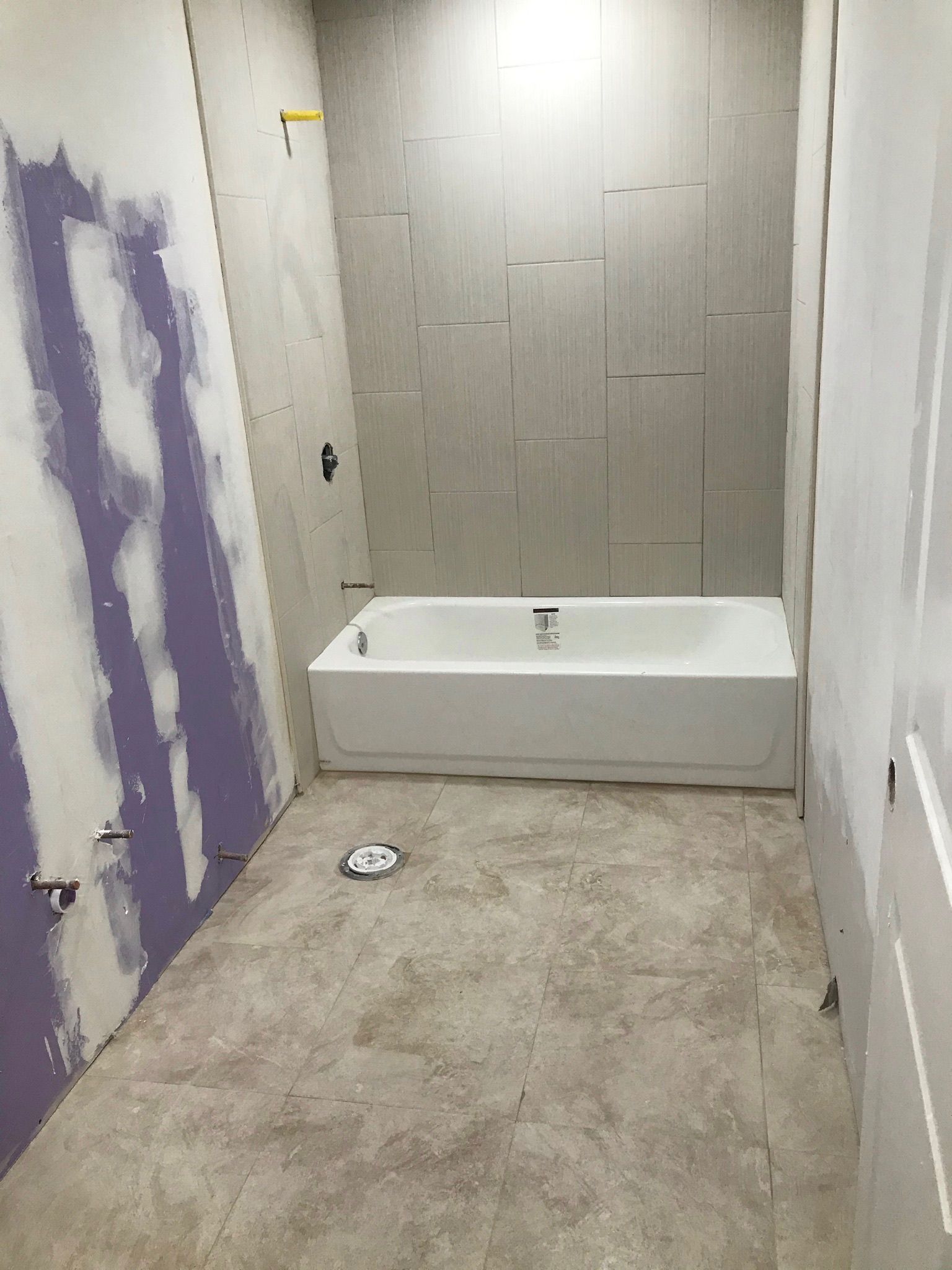 Bathroom under construction: tub, tiled wall, drywall, plumbing, and bare floor.