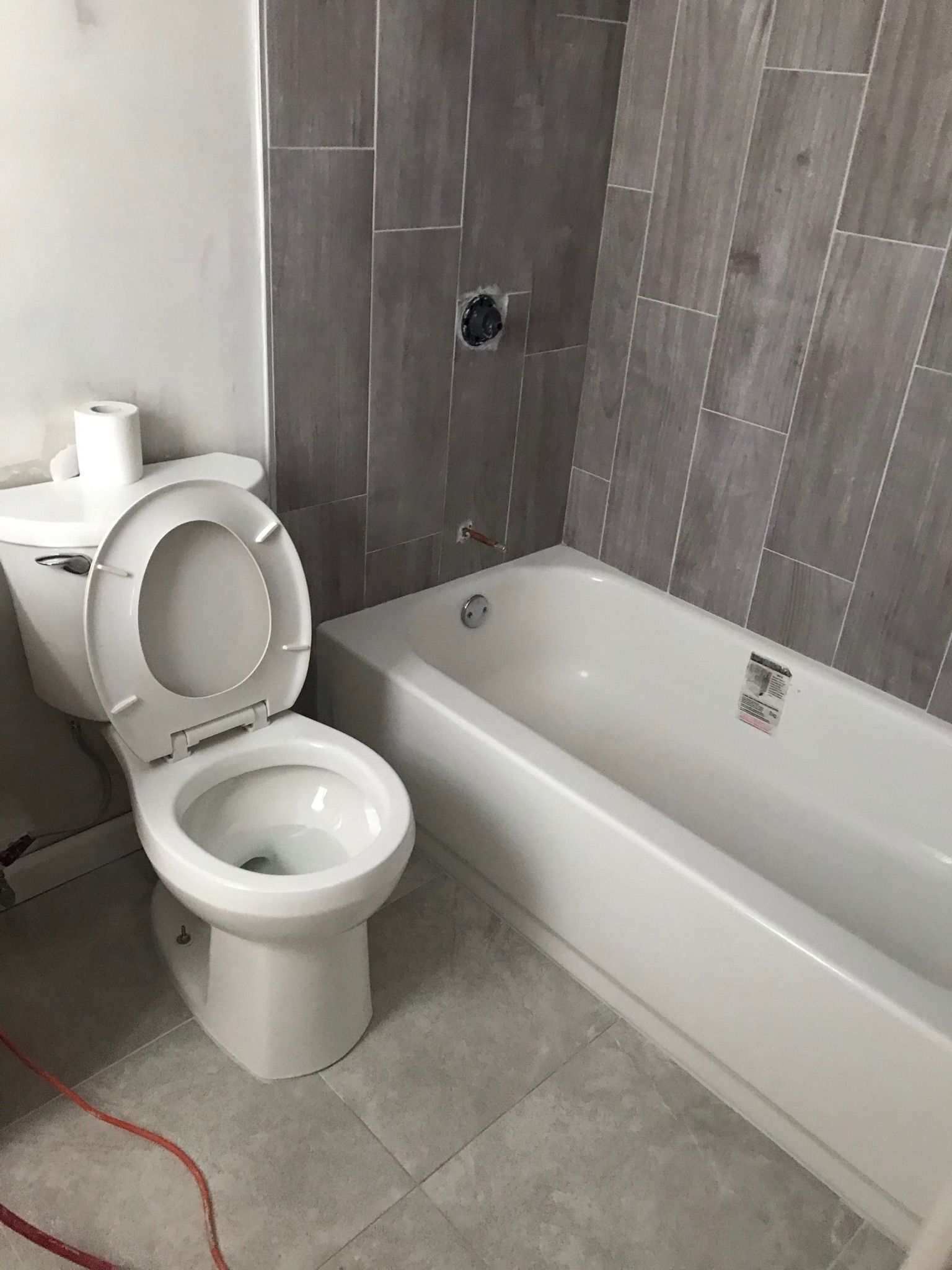 White toilet and bathtub in a bathroom with gray tiled walls and floor; partially built.
