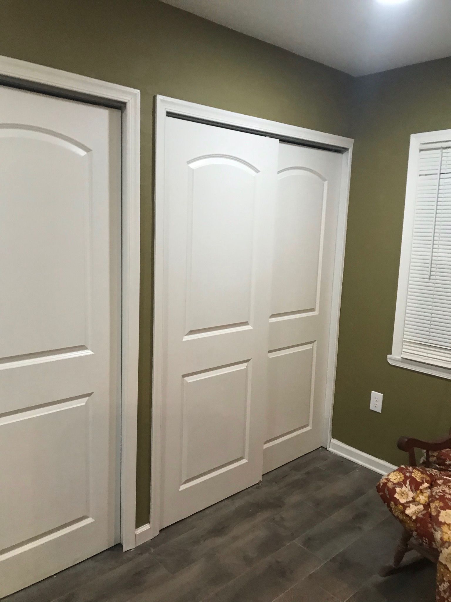 White closet doors on a green wall, next to a closed door. A window is visible.