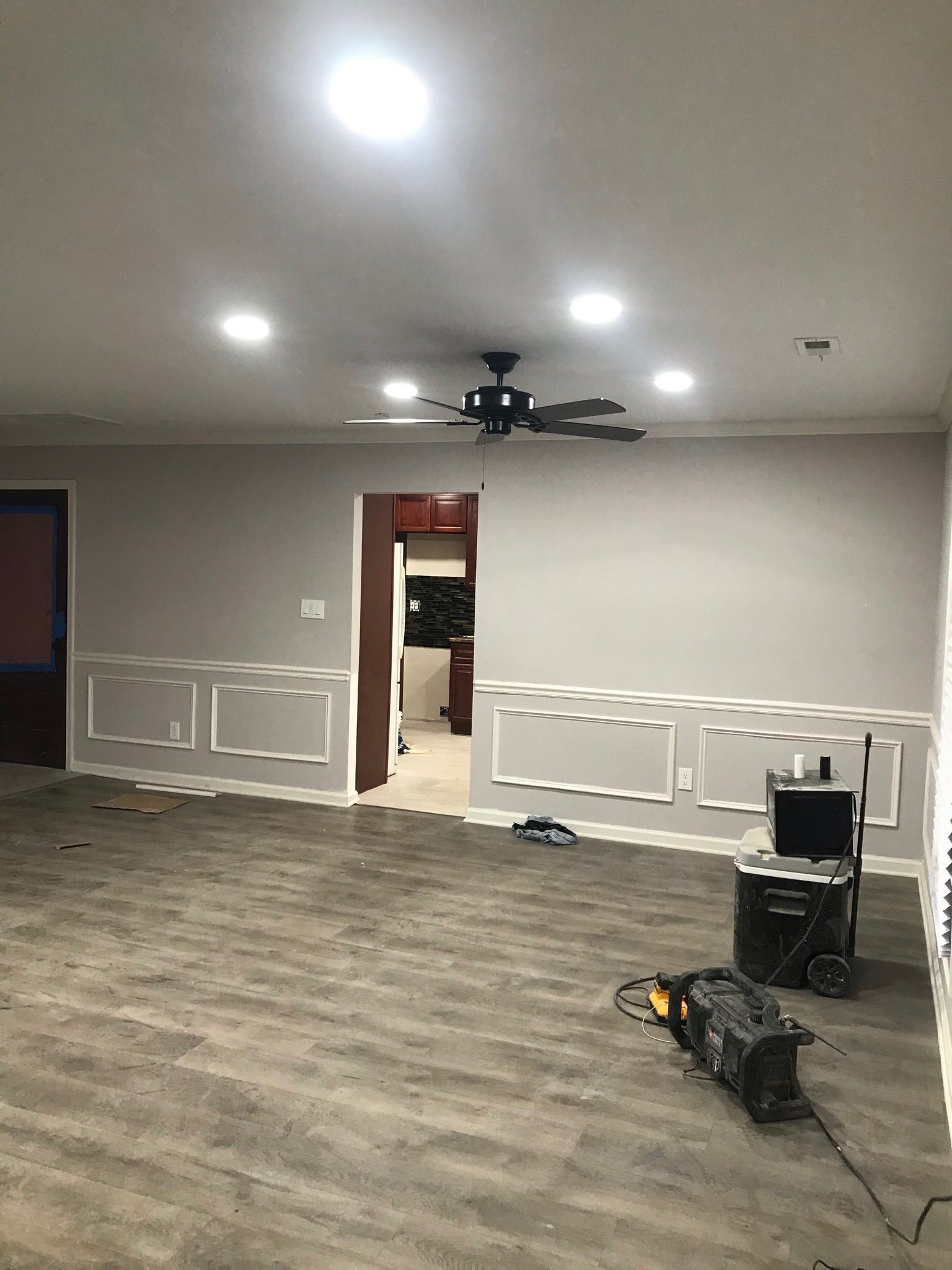 Empty room with grey walls, white trim, and wood-look flooring. Ceiling lights and fan visible.