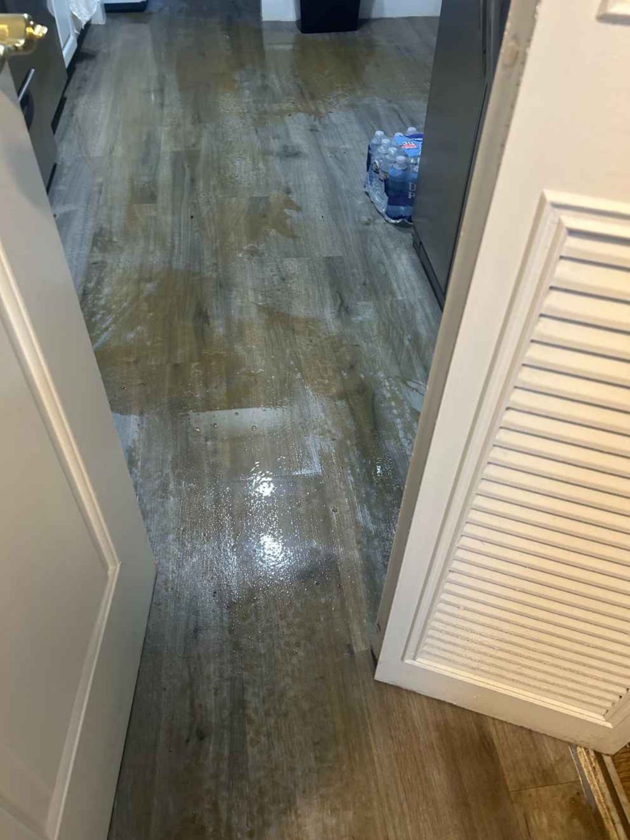 Flooded hallway with water covering the wood floor near an open louvered door.