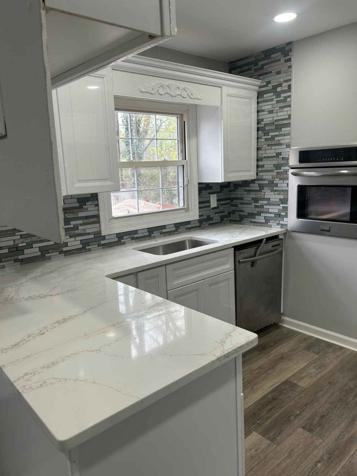 Modern kitchen with white cabinets, gray tile backsplash, marble island, and a window above the sink.
