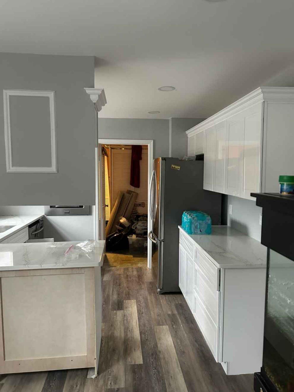 Modern kitchen with gray walls, white cabinets, stainless fridge, and a hallway cluttered with chairs in back