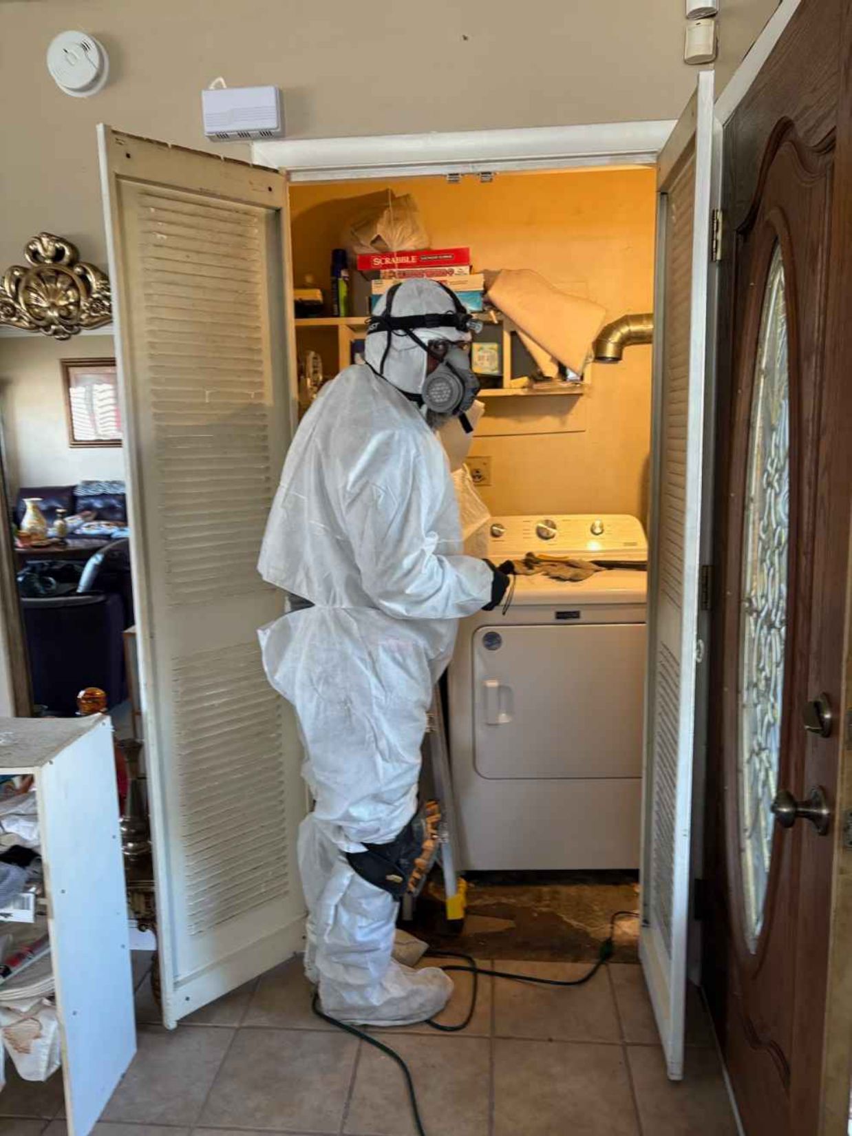 Worker in white protective suit disinfecting a kitchen sink in a small apartment.