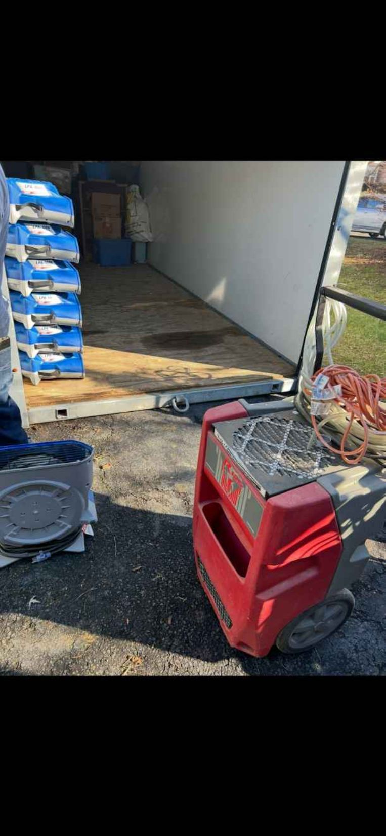 Red portable heater on gravel beside a trailer with stacked blue crates and a partially open door.