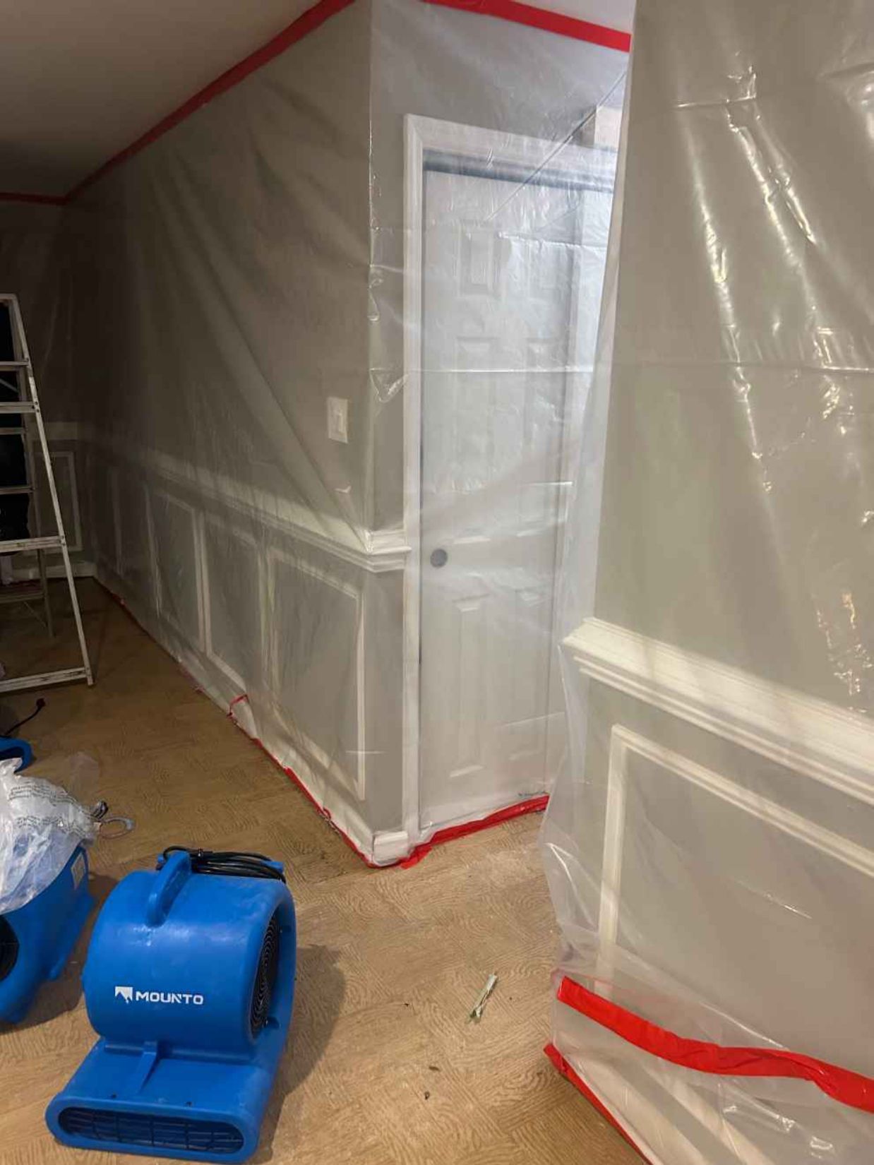 Plastic-covered room under renovation with a blue floor machine and ladder nearby.