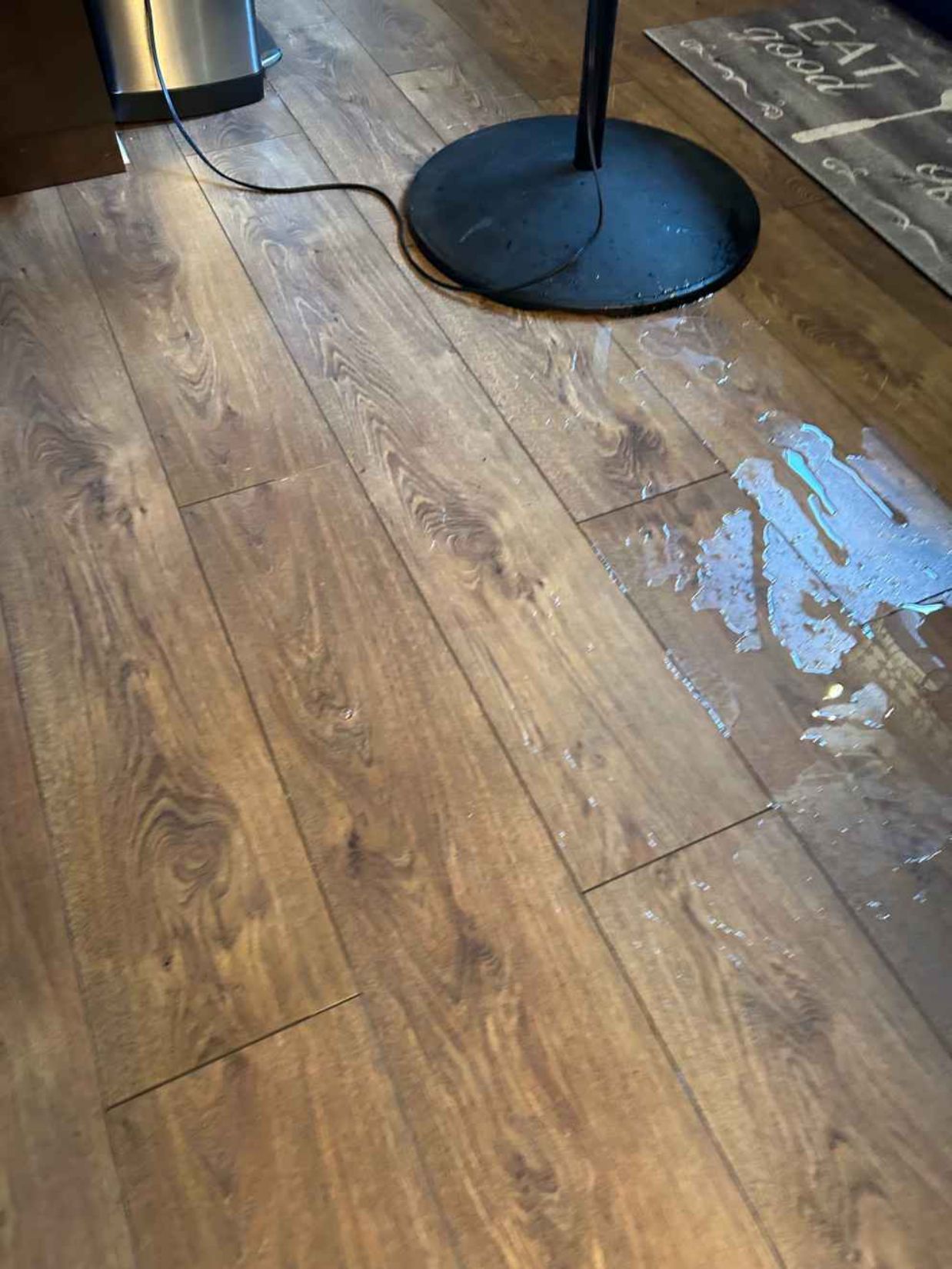 Wet wooden floor beside a black table base, with water spilled across the right side.