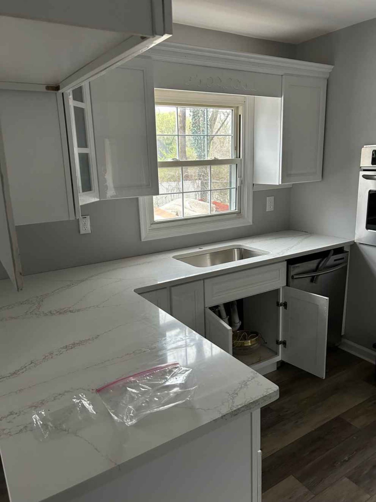 Bright white kitchen with cabinets, island, sink, and window; one lower cabinet is open under the counter.