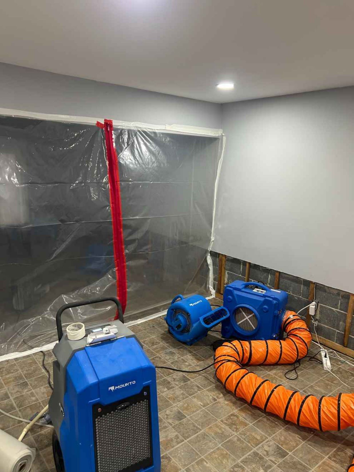 Blue industrial fans and orange ducting in a room with plastic sheeting and a dehumidifier.