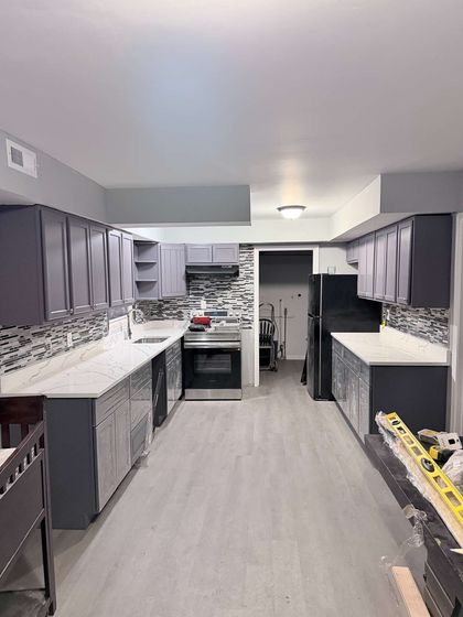 Modern kitchen under renovation with dark cabinets, white countertops, and scattered tools/boxes.