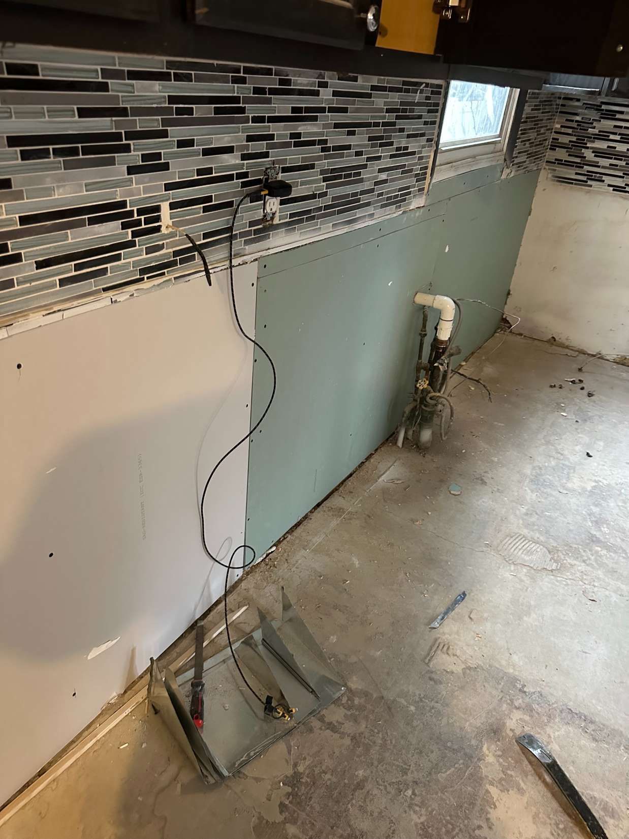 Partially renovated kitchen wall with exposed wiring, backsplash tile, and a rough concrete floor
