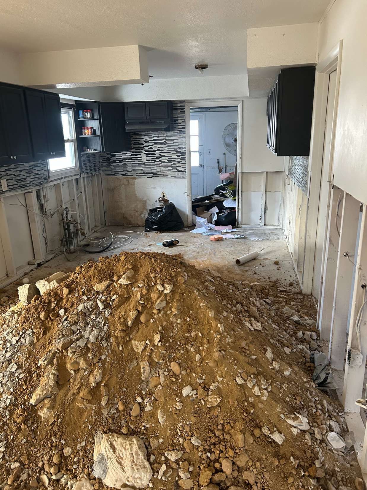 Kitchen under renovation with large dirt pile, exposed walls, and debris on the floor.