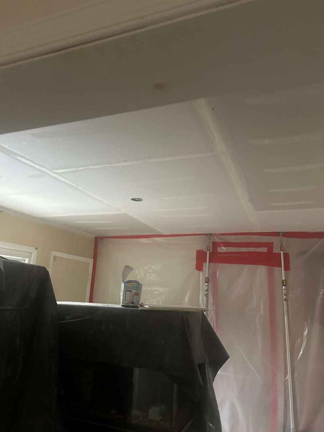 Ceiling in a room with red painter’s tape and a plastic-covered doorway above dark furniture