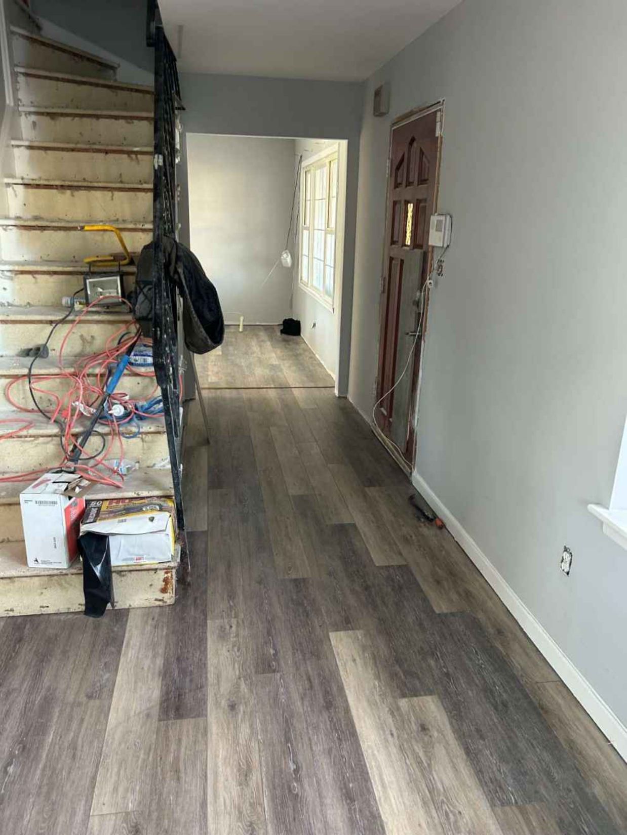 Renovated hallway with wood flooring, exposed staircase on left, and gray walls in a partly finished interior.