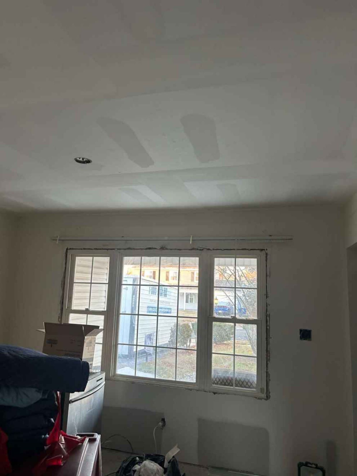 Living room under renovation with a window, patched ceiling, and construction materials on the left