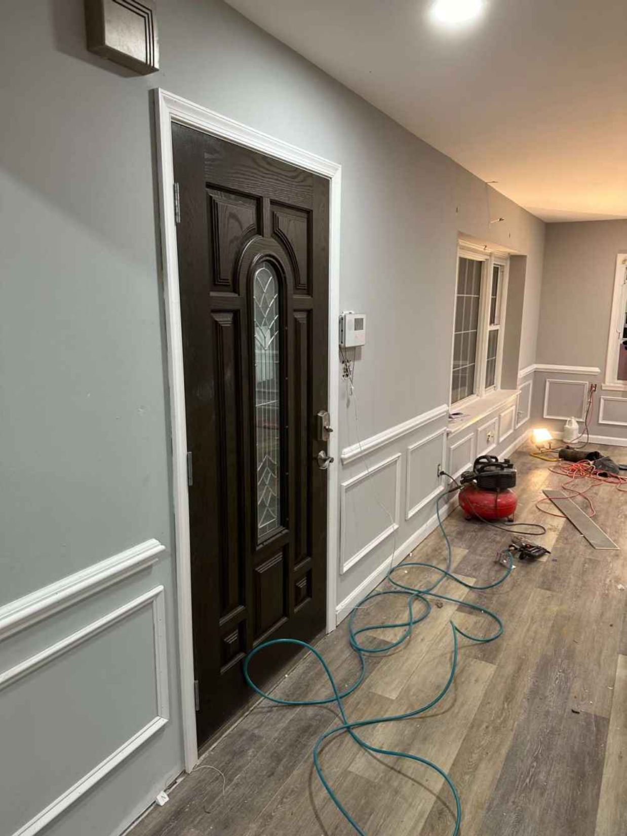 Hallway with white wainscoting, dark front door, and floor sanding equipment with cords and dust.
