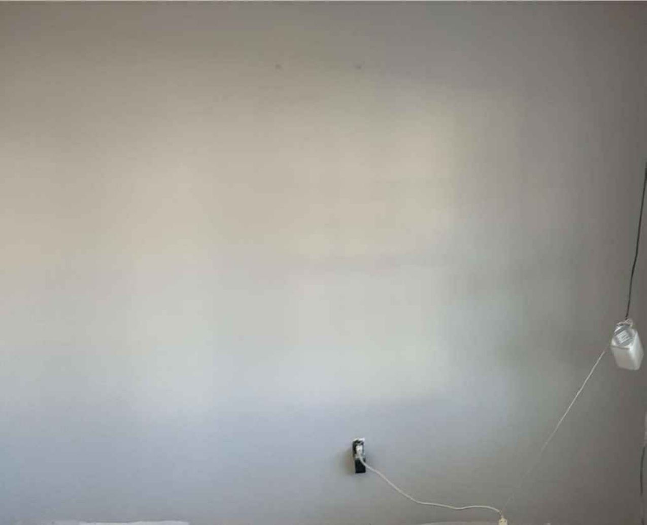 Empty light-gray wall with a hanging white cord and exposed outlet near the bottom center