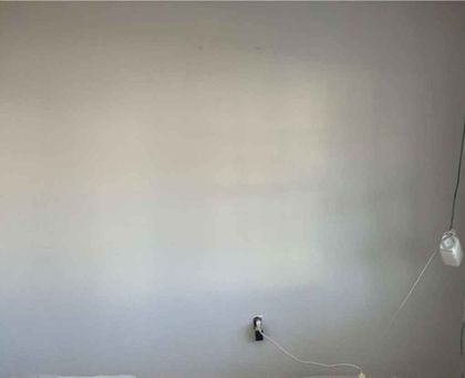 Bare white wall with a wall outlet and a hanging cable on the right side.
