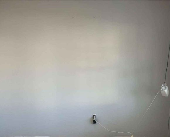 Bare white wall with a wall outlet and a hanging cable on the right side.
