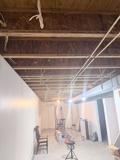Partially renovated hallway with exposed ceiling joists, white walls, chairs, tools, and construction debris.