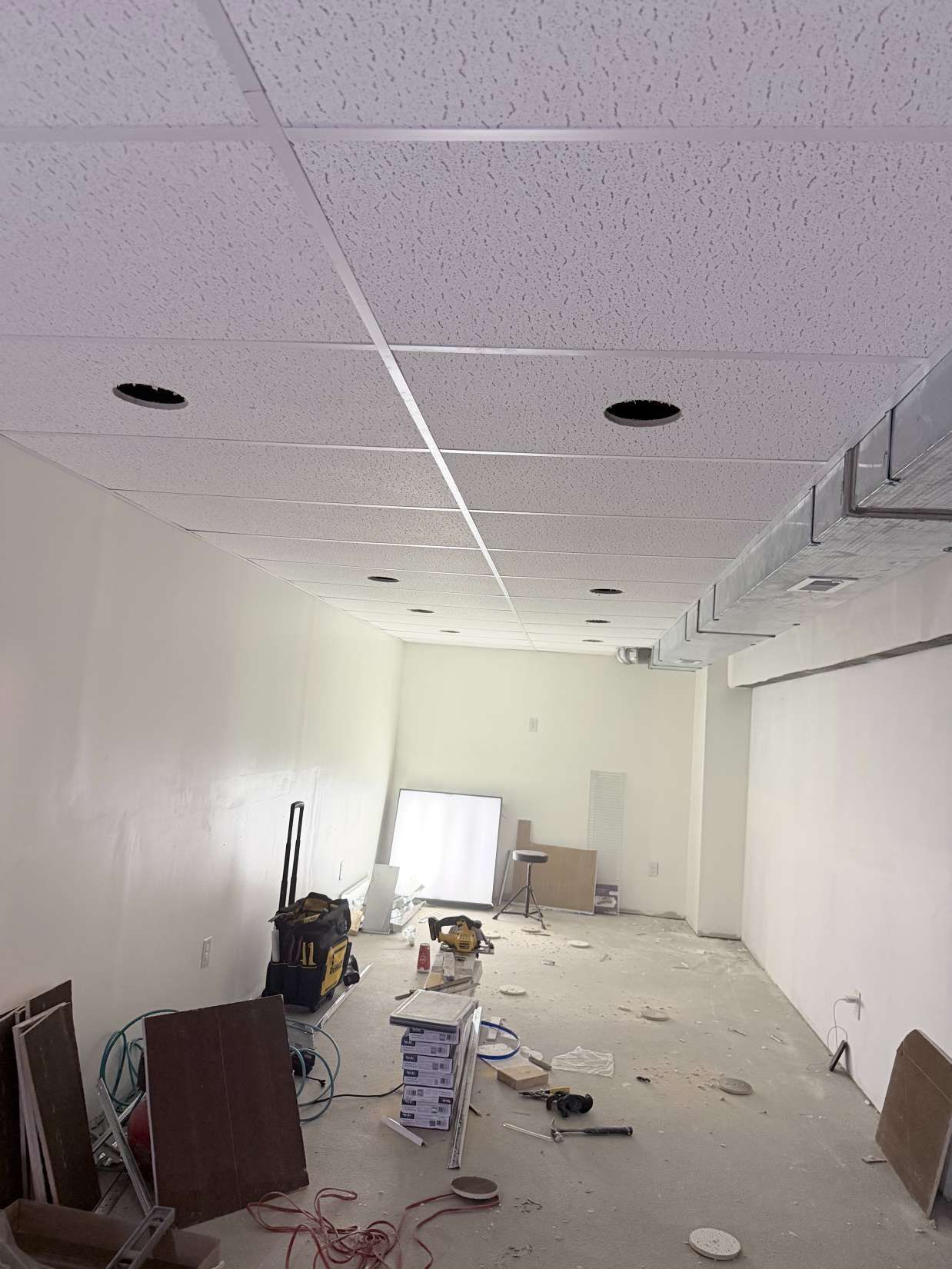 Messy office hallway under renovation, with debris scattered on the floor and ceiling tiles missing