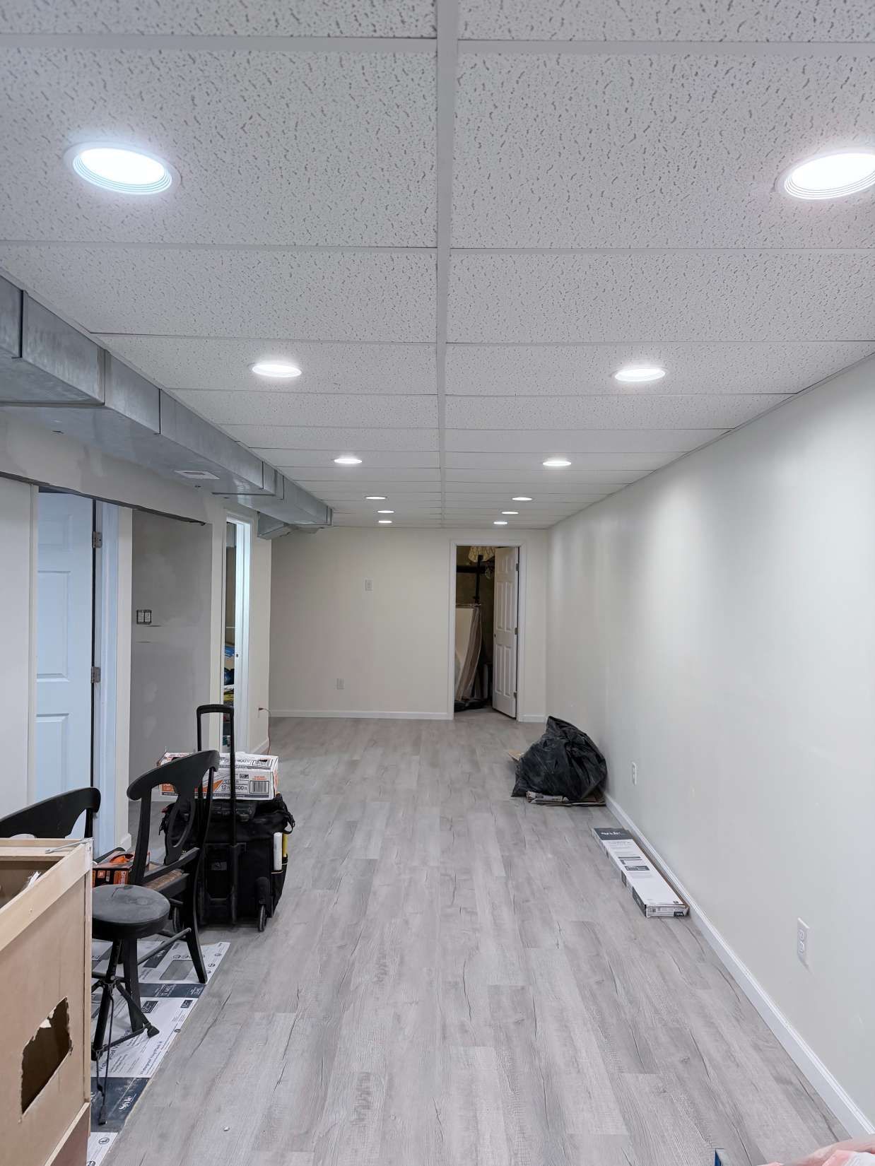 Empty hallway with white walls, recessed lights, and scattered tools on a light wood floor