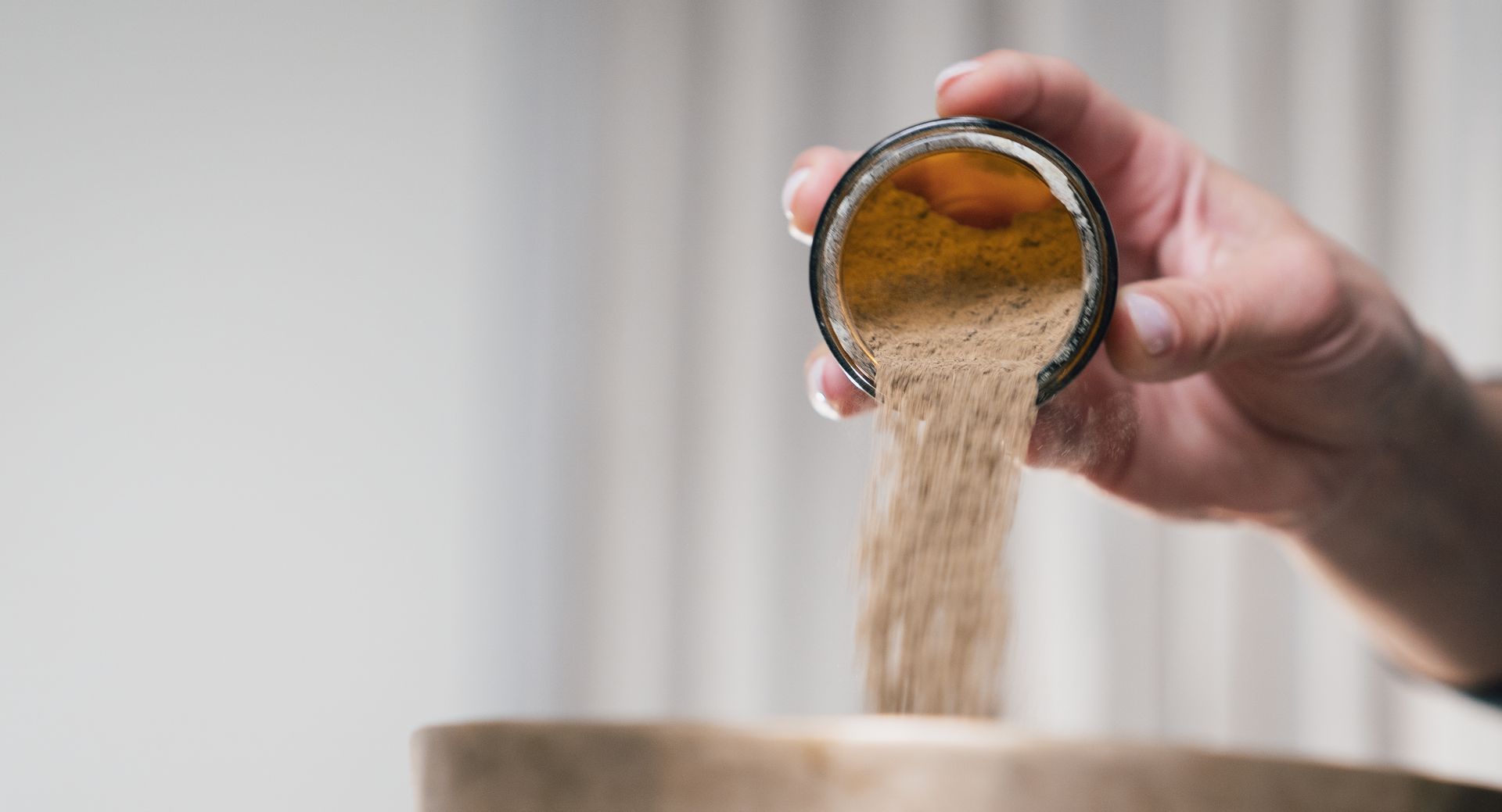 Beige Körner werden von Hand aus einem Metallbecher in eine Schüssel geschüttet.